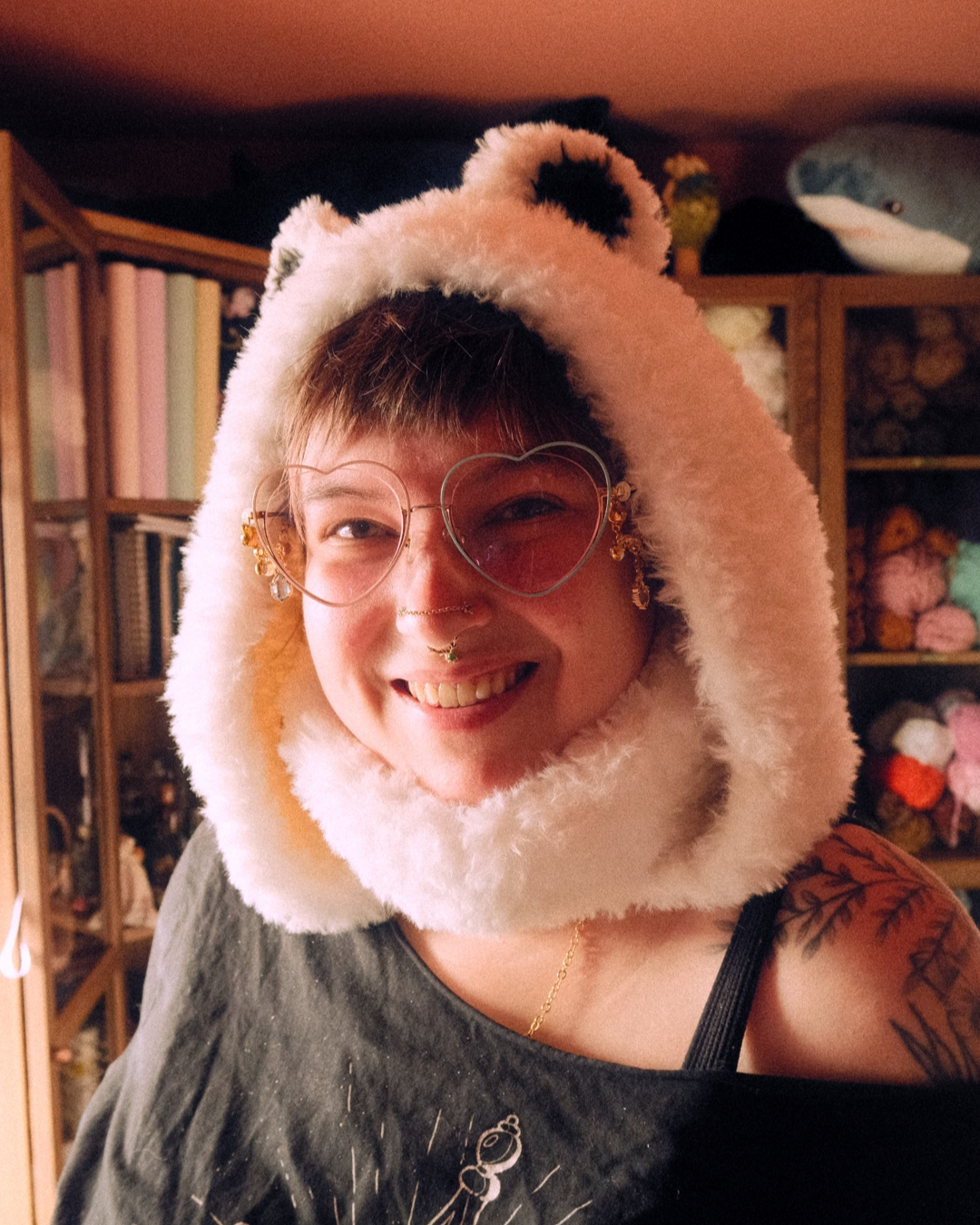 Person wearing a fluffy hood with bear ears in a room with shelves and toys.