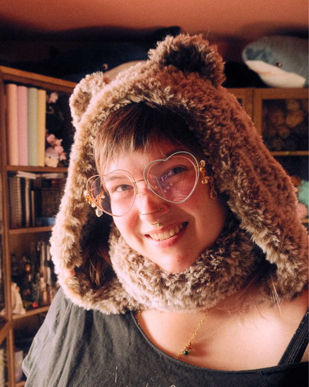 Person wearing a fluffy brown hood with bear ears in a room with bookshelves.