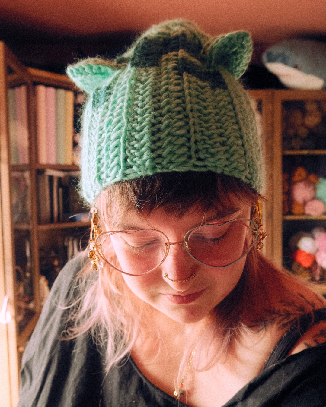 Person wearing a green crochet hat with gently pointed ears in a cozy room.