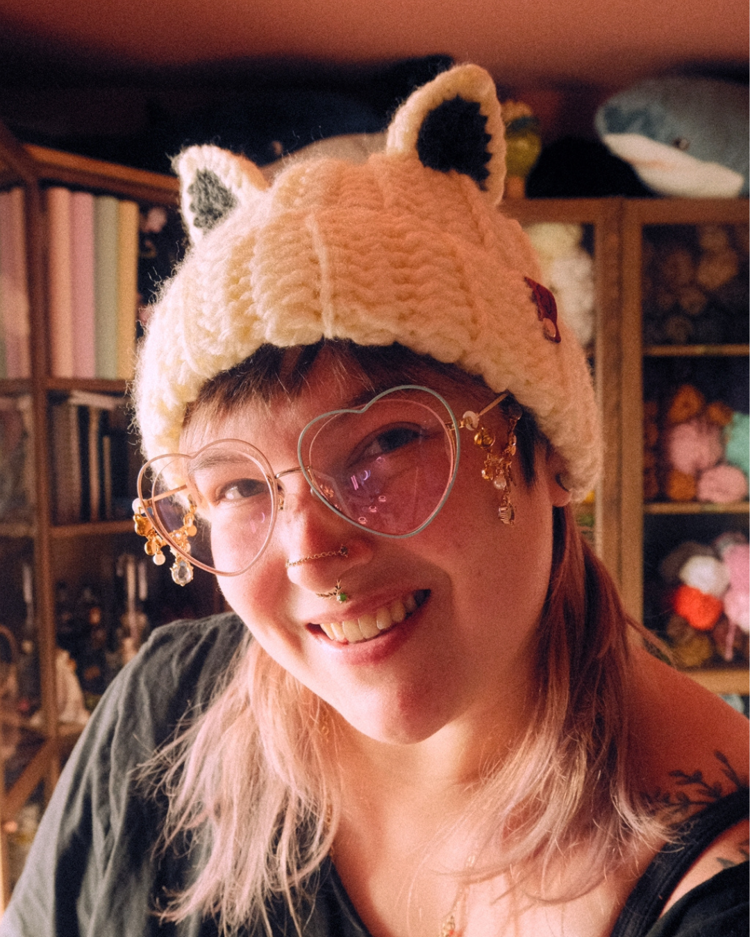 Person wearing a crochet arctic fox hat with ears in a cozy room filled with yarn and knitting supplies.