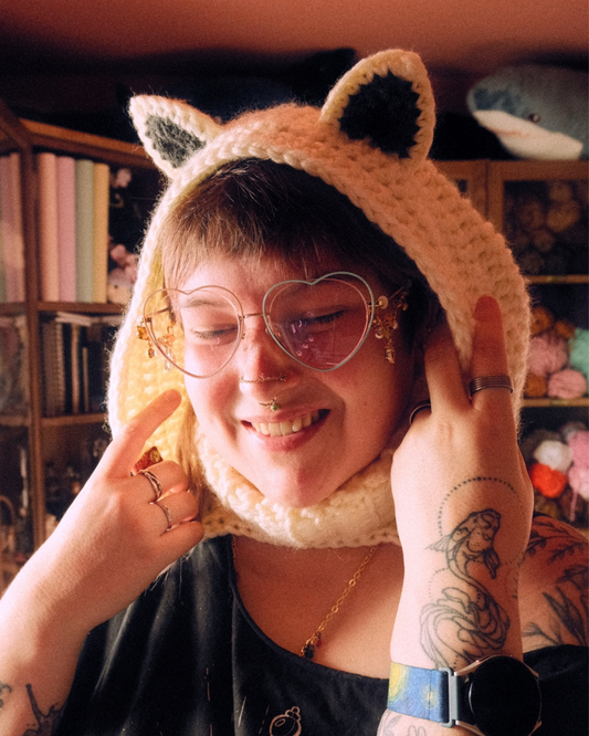 Person wearing a arctic fox-themed hat with ears, in front of a bookshelf.