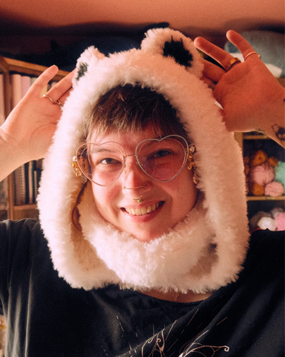 Person wearing a fluffy polar bear hood with large glasses, in a casual indoor setting.