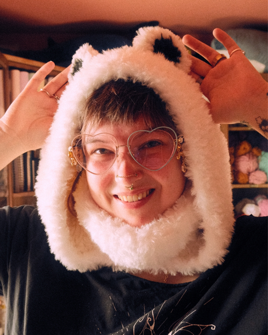Person wearing a fluffy polar bear hood with large glasses, in a casual indoor setting.