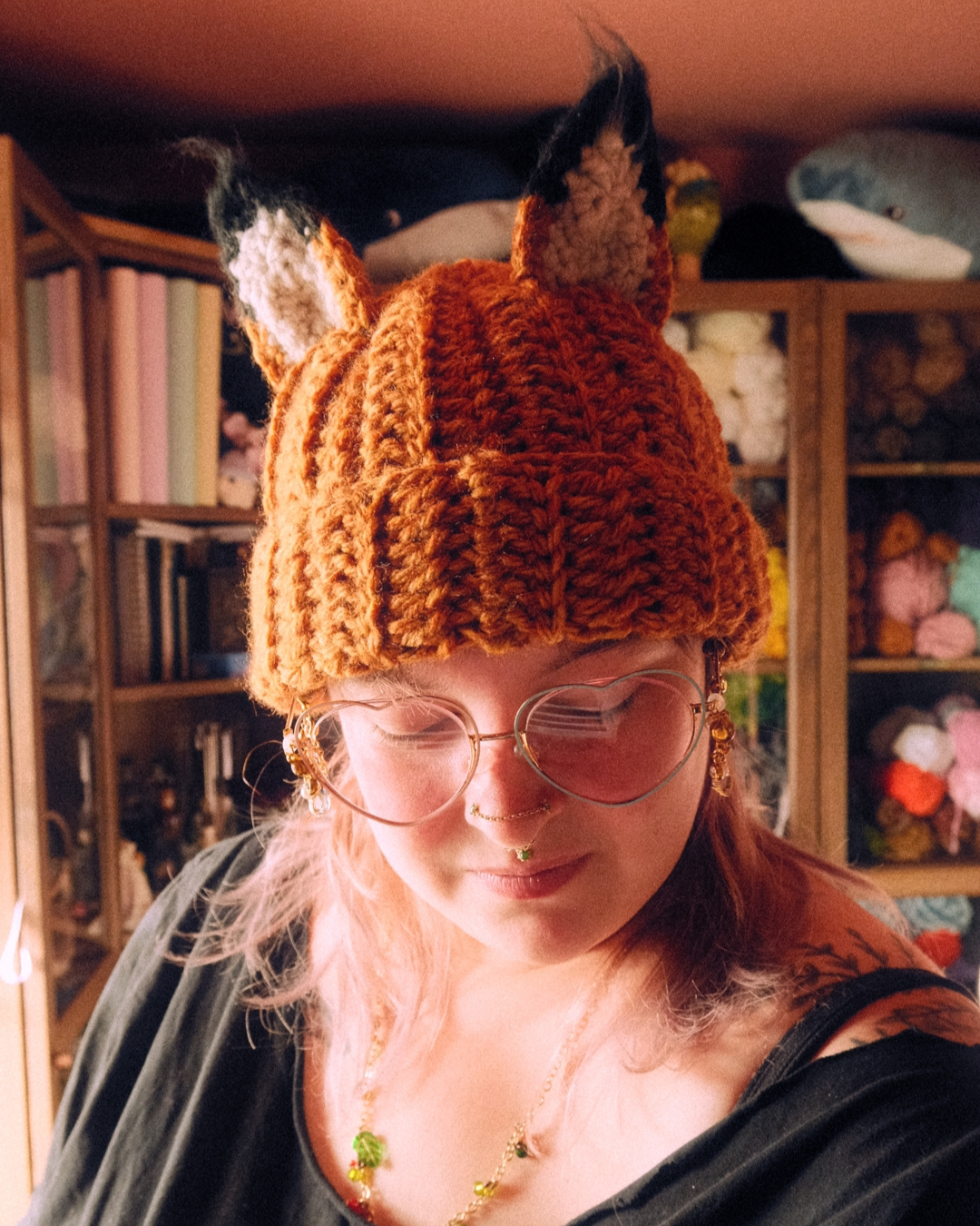 Person wearing a crochet fox hat in a cozy room with bookshelves and toys.