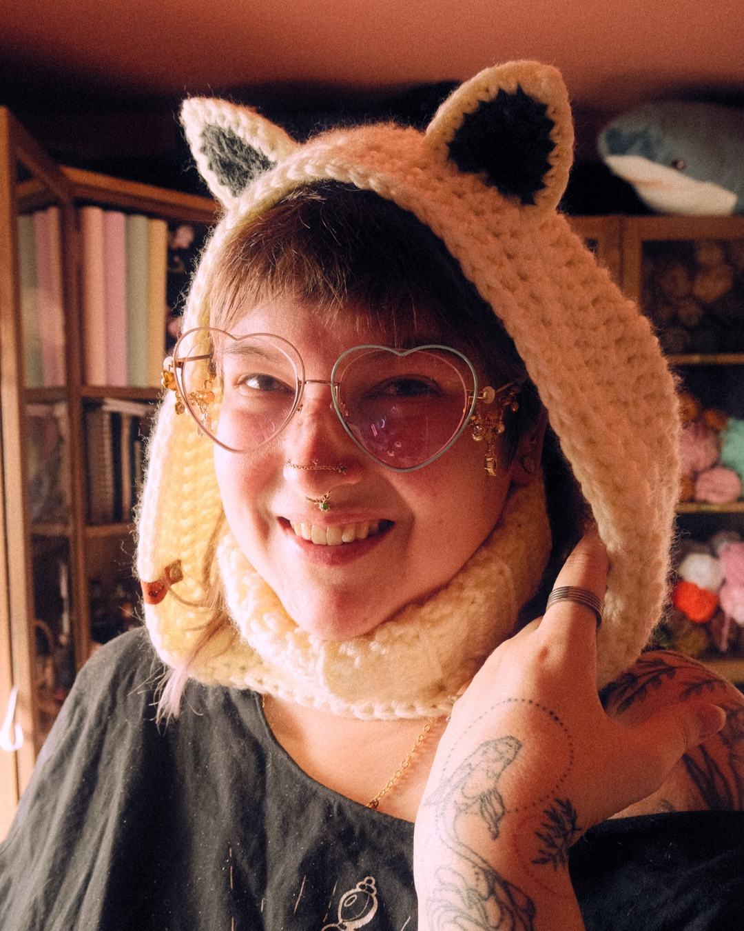 Person wearing a crochet cat hood with heart-shaped glasses in a cozy room.