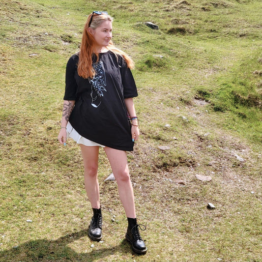 Model Cait wears a black size 4xl tshirt as an oversized tshirt dress. The artwork is a white ink drawing of a hand holding a wheel of fortune tarot card.