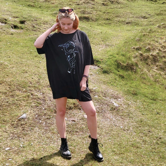 Model Cait wears a black size 4xl tshirt as an oversized tshirt dress. The artwork is a white ink drawing of a hand reaching for a crescent moon